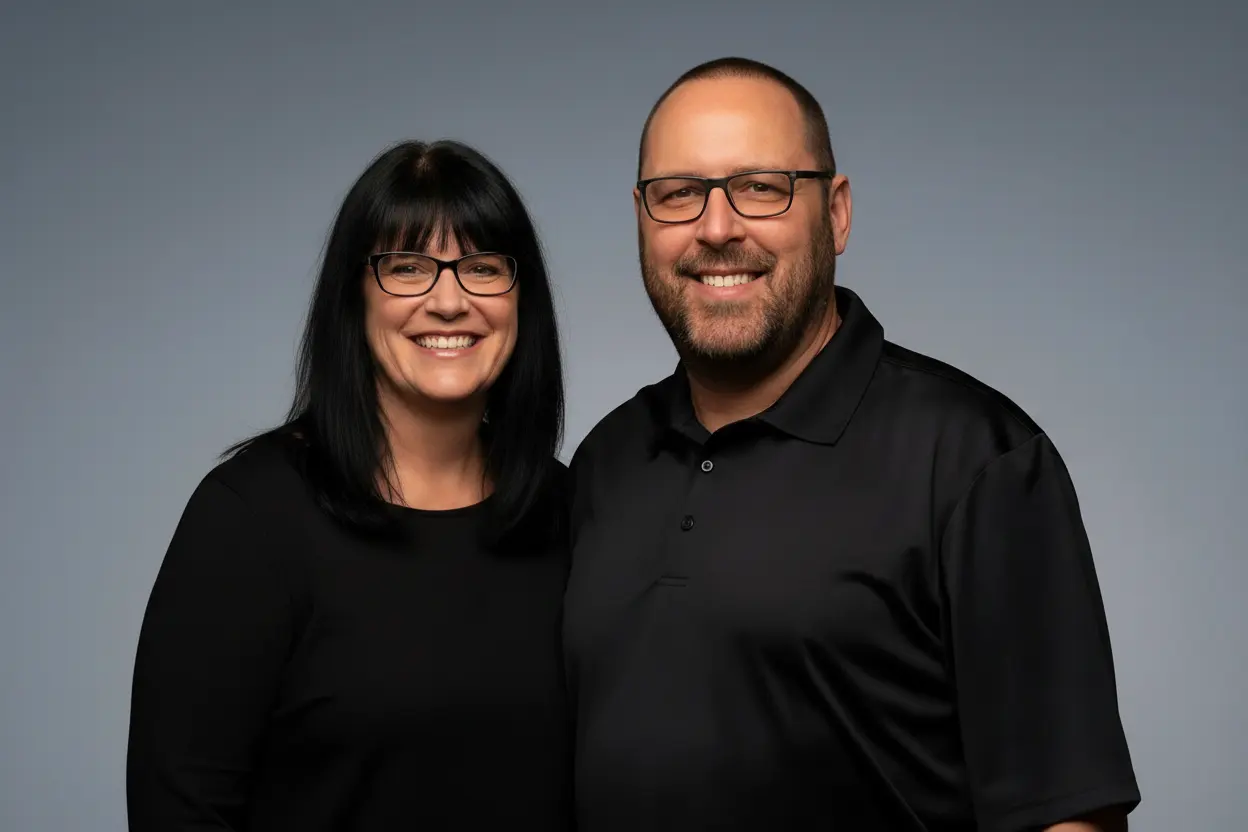 Dave and Sandra Kreider standing side by side in black work shirts against a plain gray backdrop, both smiling at the camera